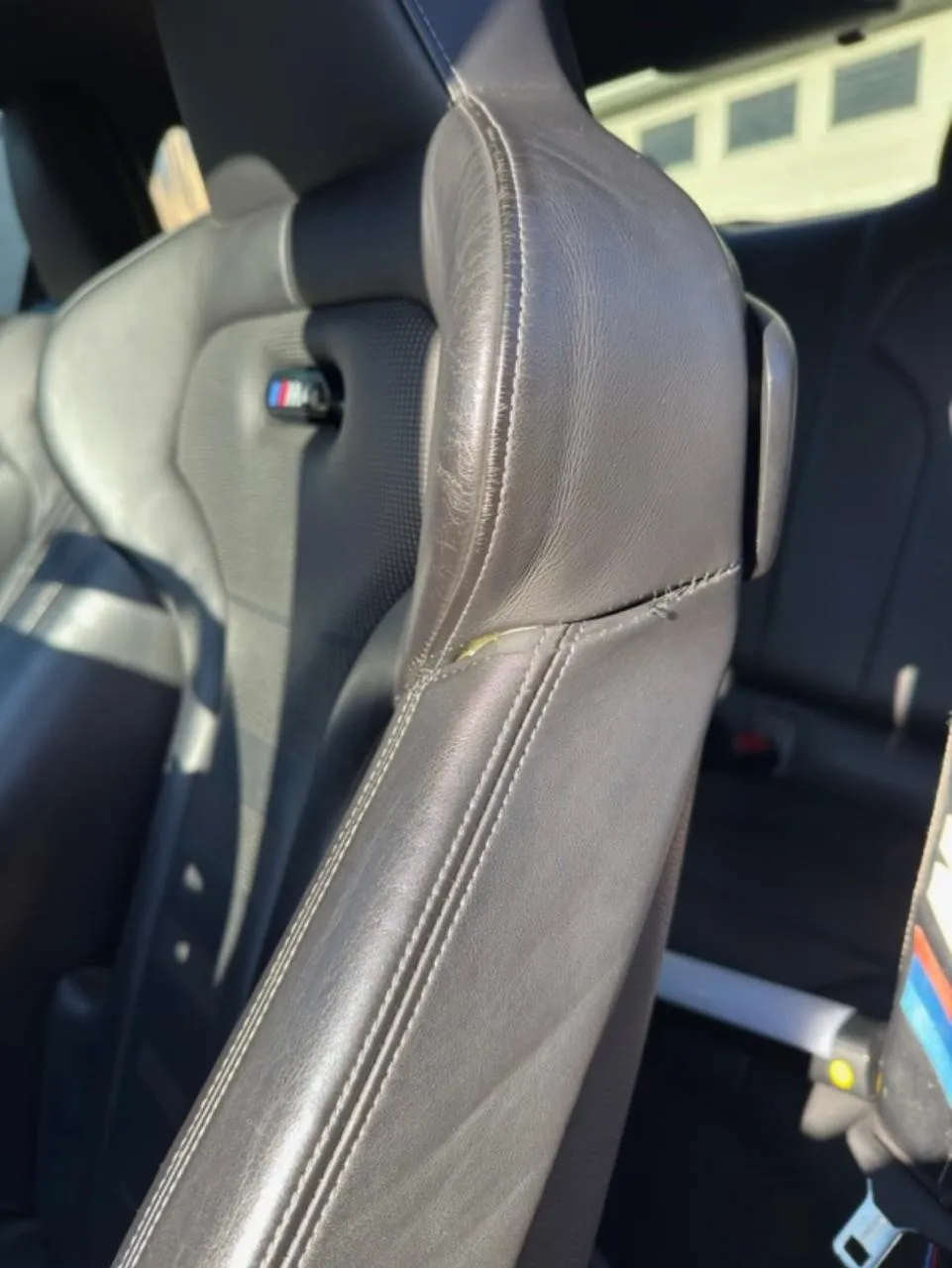 Worn edge and split seam on the bolster of a black leather car seat