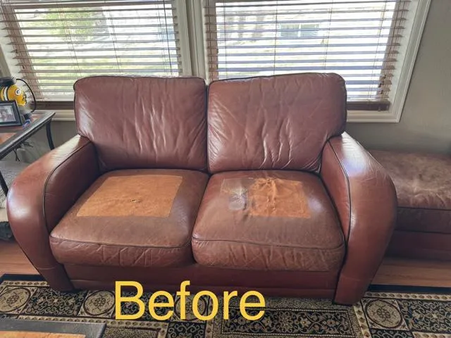 Brown leather loveseat with seat cushions worn to a light tan and a peeling patch